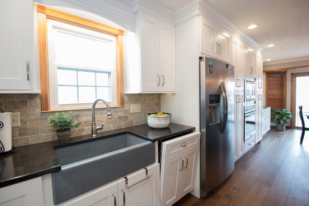 Eat-in kitchen - large transitional l-shaped medium tone wood floor eat-in kitchen idea with an undermount sink, shaker cabinets, white cabinets, granite countertops, gray backsplash, stone tile backsplash, stainless steel appliances and an island