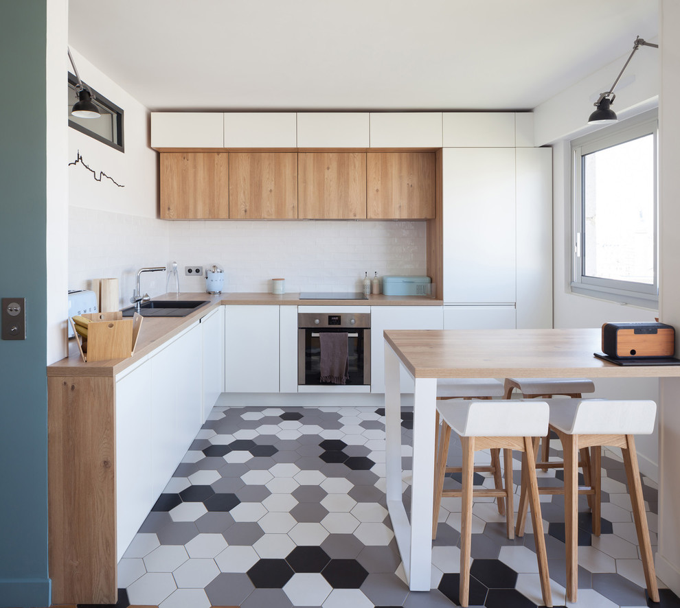 Inspiration for a mid-sized scandinavian l-shaped eat-in kitchen in Paris with a single-bowl sink, beaded inset cabinets, white cabinets, wood benchtops, white splashback, terra-cotta splashback, panelled appliances, terra-cotta floors, no island and grey floor.