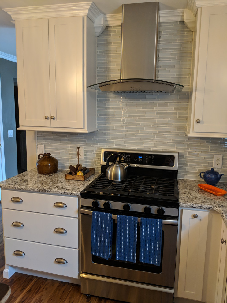 This is an example of a small transitional u-shaped eat-in kitchen in New York with an undermount sink, shaker cabinets, white cabinets, quartz benchtops, blue splashback, glass tile splashback, stainless steel appliances, medium hardwood floors, no island, multi-coloured floor and white benchtop.