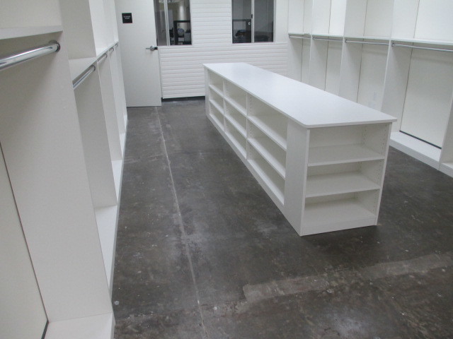 Photo of a large modern gender-neutral dressing room in Los Angeles with flat-panel cabinets, white cabinets, concrete floors and grey floor.