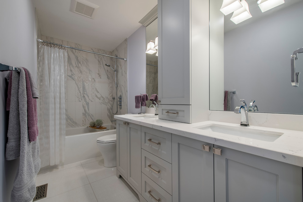 This is an example of a mid-sized contemporary master bathroom in Toronto with beaded inset cabinets, grey cabinets, an alcove tub, a shower/bathtub combo, gray tile, white tile, marble, an undermount sink, marble benchtops, a shower curtain, white benchtops, a one-piece toilet, grey walls, porcelain floors and white floor.