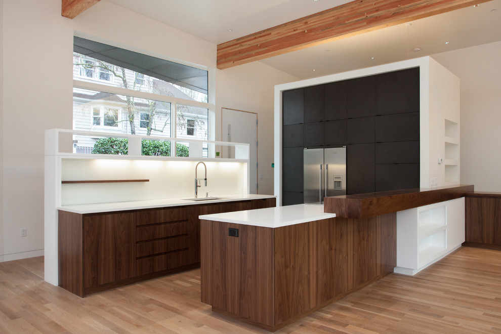 This is an example of a mid-sized modern u-shaped eat-in kitchen in Portland with flat-panel cabinets, black cabinets, white splashback, stainless steel appliances, an undermount sink, solid surface benchtops, medium hardwood floors, a peninsula and beige floor.