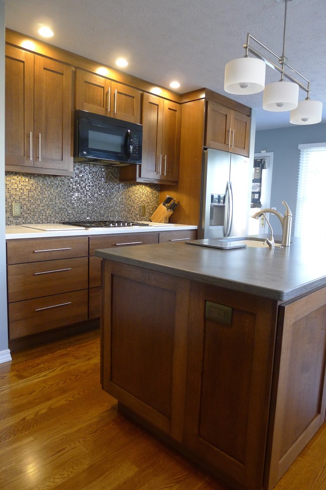 This is an example of a mid-sized transitional u-shaped eat-in kitchen in Indianapolis with an integrated sink, shaker cabinets, medium wood cabinets, solid surface benchtops, brown splashback, stainless steel appliances, medium hardwood floors and with island.