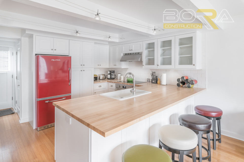 Small transitional u-shaped medium tone wood floor and beige floor eat-in kitchen photo with a double-bowl sink, shaker cabinets, white cabinets, wood countertops, white backsplash, ceramic backsplash, stainless steel appliances and a peninsula
