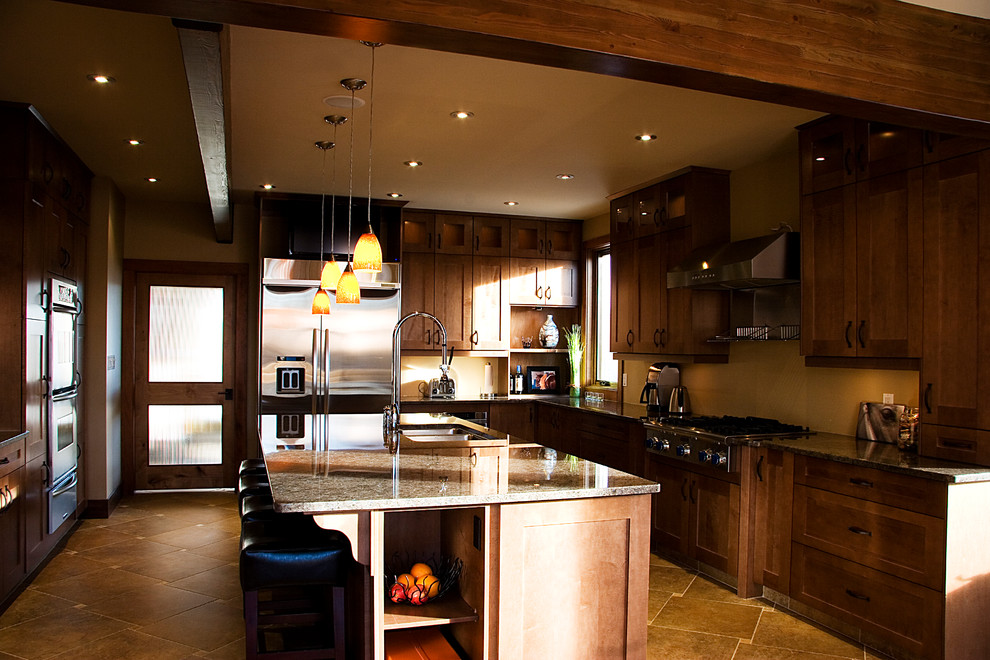 Example of a mid-sized mountain style u-shaped travertine floor enclosed kitchen design in Edmonton with an undermount sink, shaker cabinets, brown cabinets, granite countertops and an island