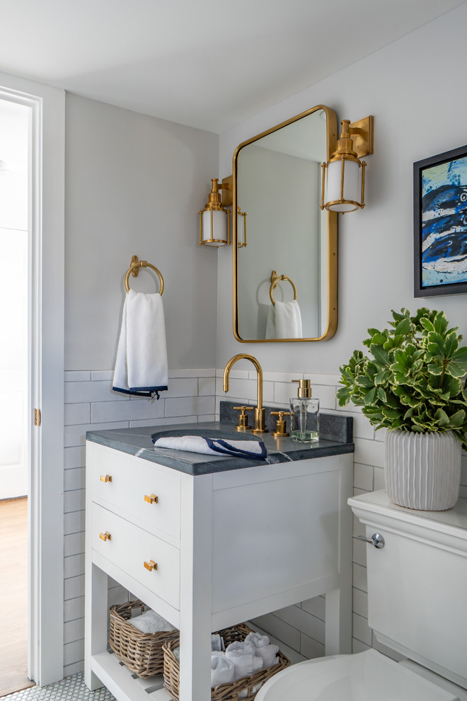 This is an example of a small beach style powder room in Boston with furniture-like cabinets, white cabinets, a two-piece toilet, white tile, grey walls, an undermount sink, marble benchtops, grey benchtops, subway tile, mosaic tile floors and white floor.
