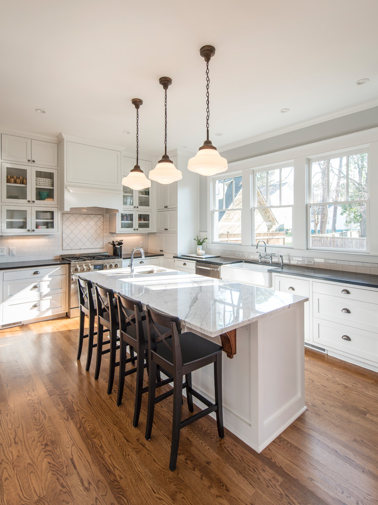 Design ideas for a mid-sized country l-shaped eat-in kitchen in Atlanta with a farmhouse sink, shaker cabinets, white cabinets, marble benchtops, white splashback, subway tile splashback, stainless steel appliances, medium hardwood floors and with island.