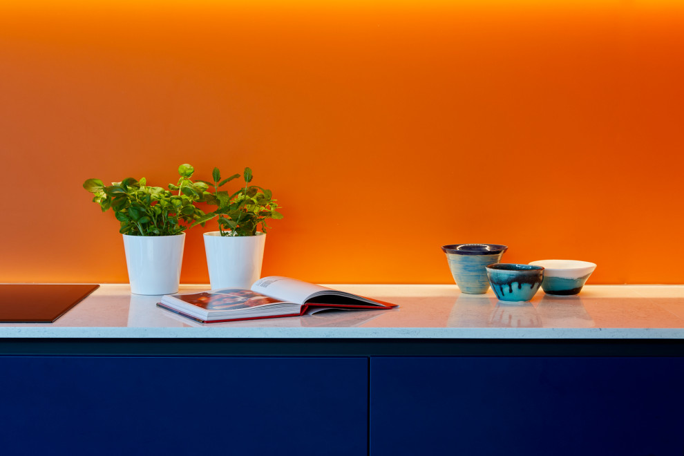 Inspiration for a large contemporary l-shaped eat-in kitchen in London with flat-panel cabinets, blue cabinets, quartzite benchtops, orange splashback, glass sheet splashback, stainless steel appliances, concrete floors, with island and grey floor.