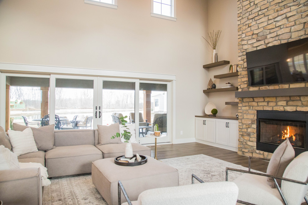 This is an example of a large traditional open concept living room in Indianapolis with beige walls, medium hardwood floors, a standard fireplace, a stone fireplace surround, a wall-mounted tv, brown floor and exposed beam.