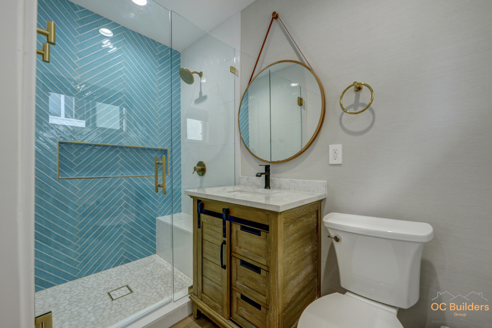 This is an example of a small beach style 3/4 bathroom in Orange County with recessed-panel cabinets, medium wood cabinets, an alcove shower, a one-piece toilet, pink tile, ceramic tile, grey walls, medium hardwood floors, an undermount sink, engineered quartz benchtops, brown floor, a hinged shower door, white benchtops, a shower seat, a single vanity and a built-in vanity.