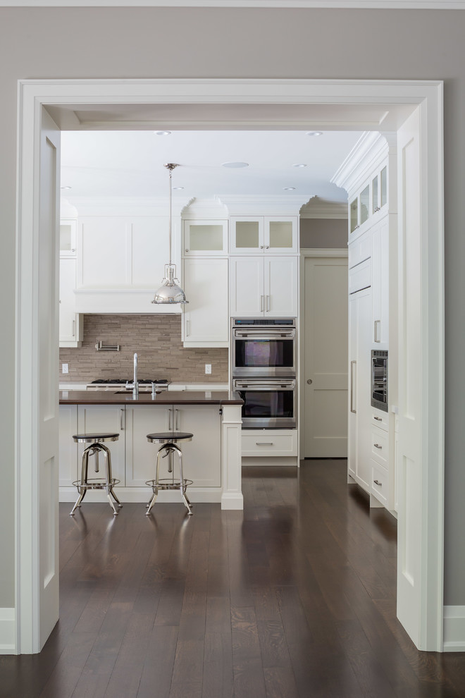 Inspiration for a large transitional medium tone wood floor enclosed kitchen remodel in Toronto with a double-bowl sink, recessed-panel cabinets, white cabinets, wood countertops, beige backsplash, stone tile backsplash, stainless steel appliances and an island