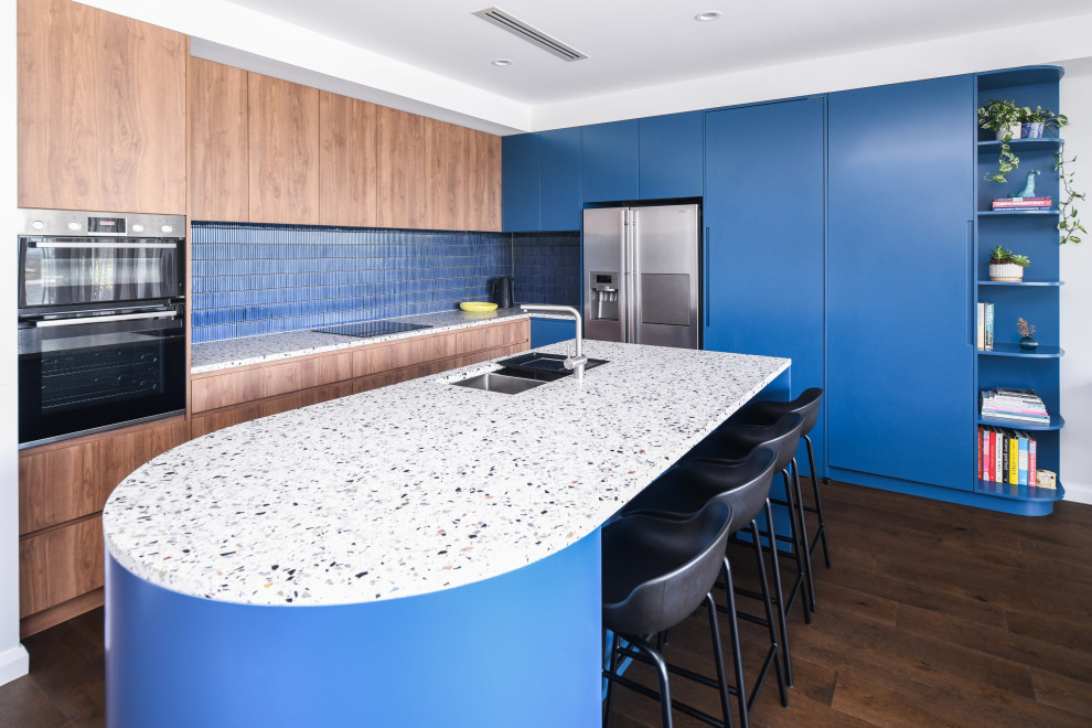 Foto på ett stort funkis flerfärgad kök, med en undermonterad diskho, blå skåp, bänkskiva i terrazo, blått stänkskydd, stänkskydd i mosaik, rostfria vitvaror, en köksö och brunt golv