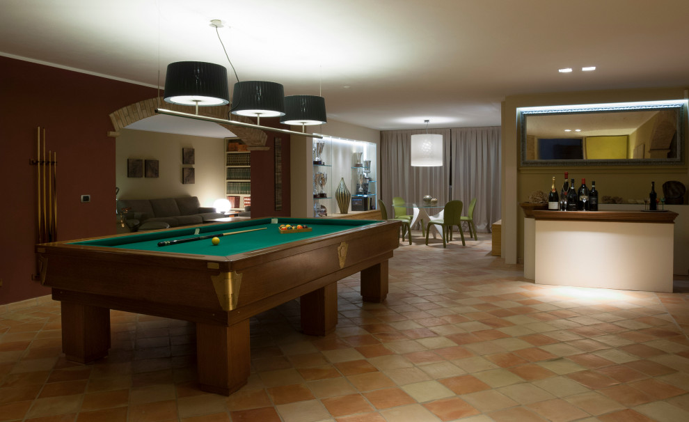 This is an example of an expansive rustic walk-out basement in Other with a game room, brown walls, terracotta flooring, orange floors and brick walls.