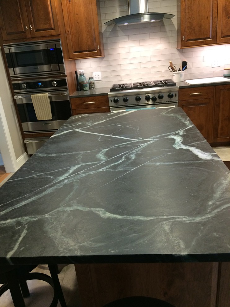Inspiration for a mid-sized rustic l-shaped porcelain tile and beige floor open concept kitchen remodel with beaded inset cabinets, medium tone wood cabinets, soapstone countertops, white backsplash, stainless steel appliances and an island