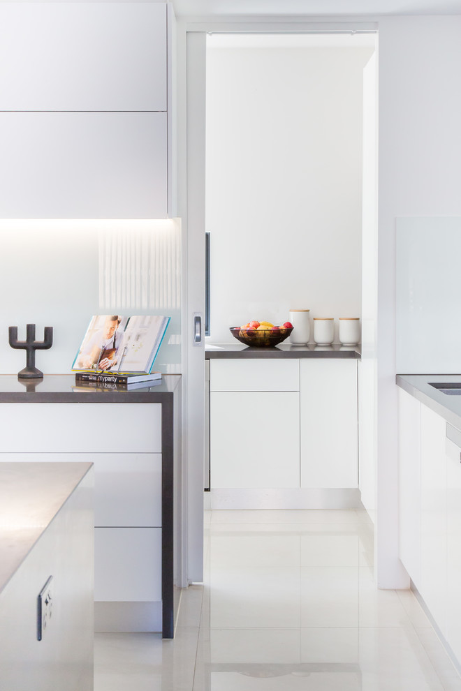 Photo of a mid-sized contemporary single-wall open plan kitchen in Melbourne with a drop-in sink, flat-panel cabinets, white cabinets, concrete benchtops, white splashback, glass sheet splashback, stainless steel appliances, ceramic floors, with island, white floor and grey benchtop.