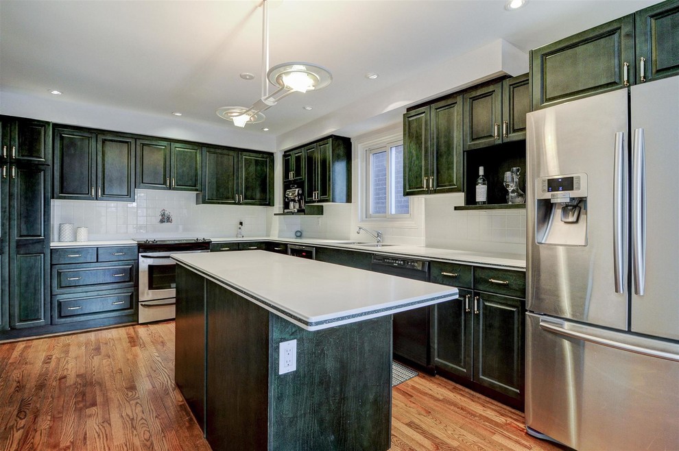 Enclosed kitchen - large transitional l-shaped medium tone wood floor and brown floor enclosed kitchen idea in Toronto with a double-bowl sink, recessed-panel cabinets, green cabinets, laminate countertops, white backsplash, ceramic backsplash, stainless steel appliances and an island