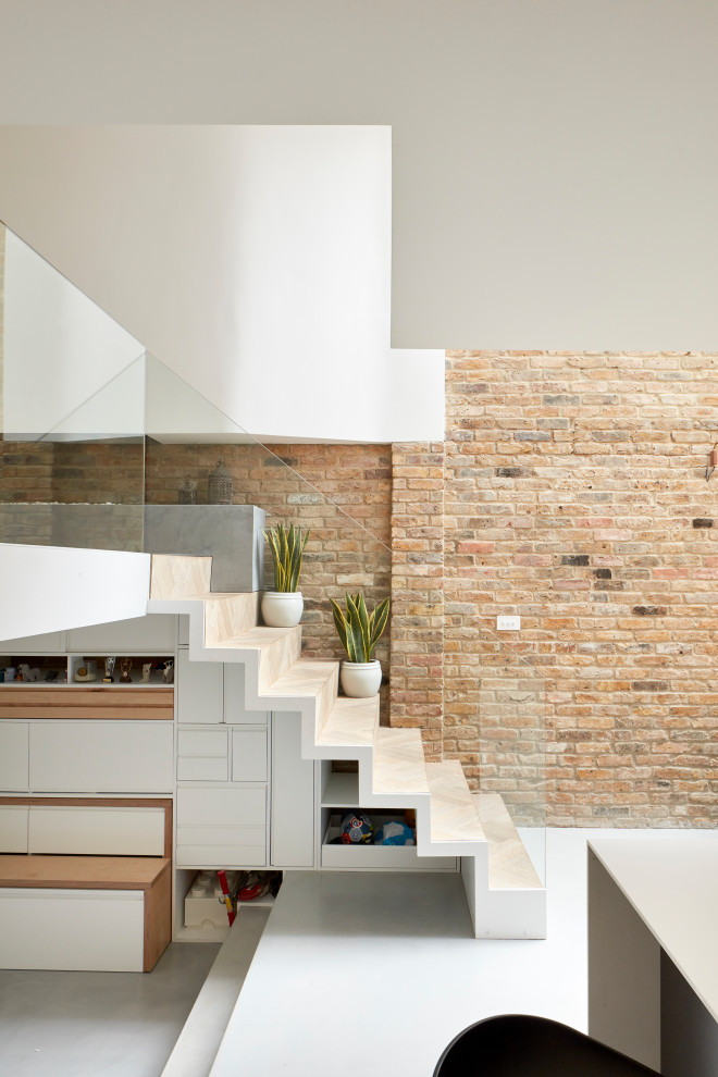 Exemple d'un escalier droit tendance avec un garde-corps en verre et un mur en parement de brique.