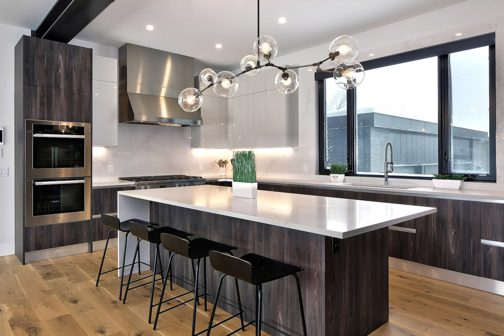 This is an example of a large contemporary l-shaped eat-in kitchen in Toronto with a single-bowl sink, flat-panel cabinets, quartz benchtops, white splashback, stone slab splashback, stainless steel appliances, light hardwood floors, with island, dark wood cabinets, beige floor and white benchtop.