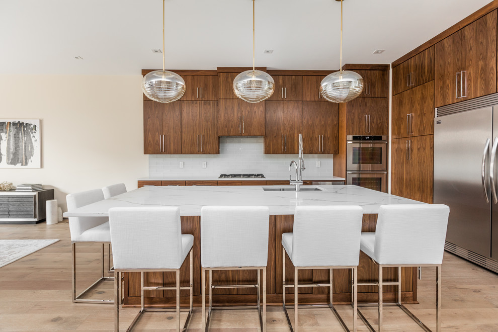 Contemporary open plan kitchen in Indianapolis with an undermount sink, flat-panel cabinets, medium wood cabinets, white splashback, subway tile splashback, stainless steel appliances, light hardwood floors, with island, beige floor and white benchtop.