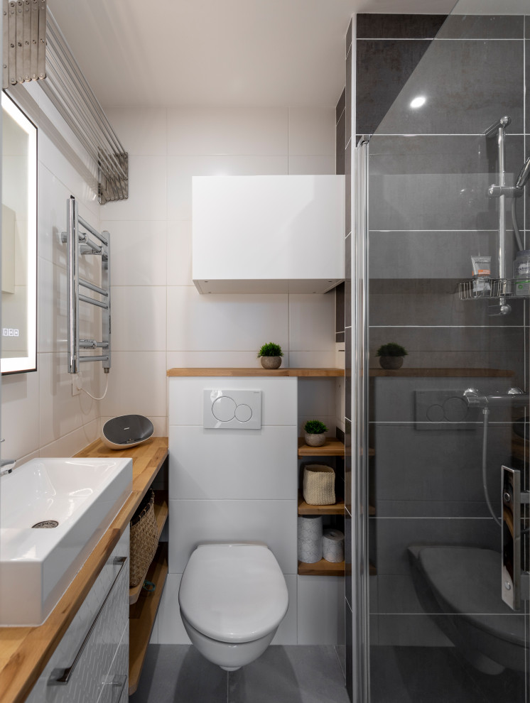 This is an example of a small industrial 3/4 bathroom in Paris with flat-panel cabinets, white cabinets, an alcove shower, a wall-mount toilet, white tile, ceramic tile, white walls, ceramic floors, a drop-in sink, wood benchtops, grey floor, a hinged shower door, brown benchtops, a single vanity and a floating vanity.