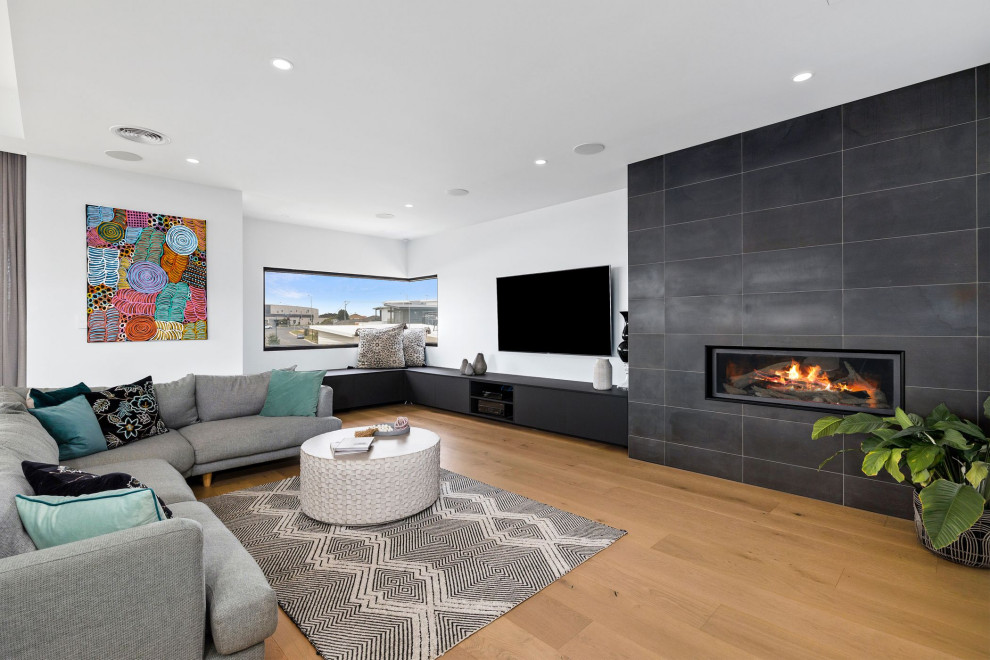 Large contemporary open concept living room in Geelong with white walls, light hardwood floors, a standard fireplace, a tile fireplace surround and a wall-mounted tv.