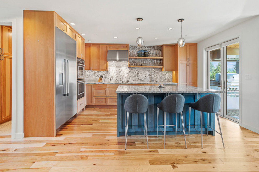 Inspiration for a mid-sized transitional l-shaped open plan kitchen in Seattle with an undermount sink, shaker cabinets, medium wood cabinets, granite benchtops, grey splashback, granite splashback, stainless steel appliances, medium hardwood floors, with island, grey benchtop and brown floor.