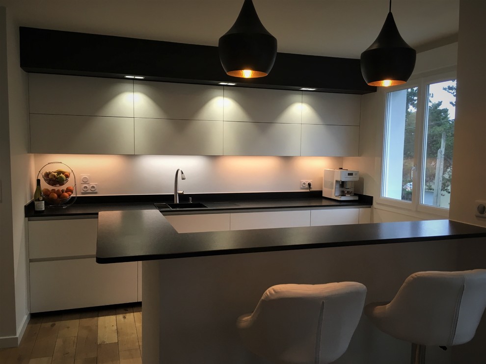 Inspiration for a mid-sized contemporary galley eat-in kitchen in Other with an undermount sink, flat-panel cabinets, white cabinets, granite benchtops, black splashback, light hardwood floors, a peninsula and black benchtop.