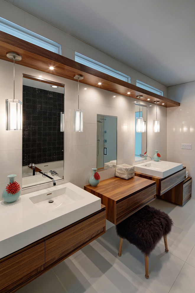 Photo of a mid-sized contemporary master bathroom in Chicago with medium wood cabinets, a freestanding tub, a curbless shower, a wall-mount toilet, white tile, black tile, porcelain tile, white walls, porcelain floors, white floor, a hinged shower door, flat-panel cabinets, an integrated sink and solid surface benchtops.
