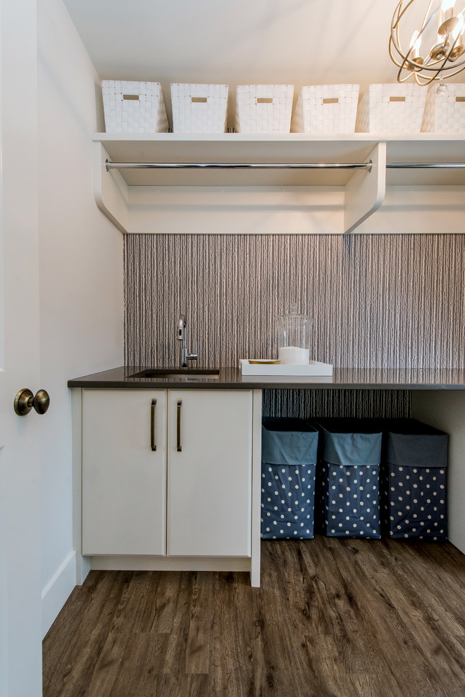 This is an example of a large contemporary galley dedicated laundry room in Calgary with an undermount sink, flat-panel cabinets, white cabinets, quartz benchtops, medium hardwood floors and white walls.