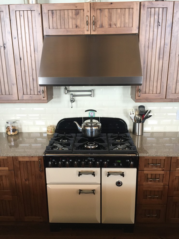 This is an example of a mid-sized country single-wall open plan kitchen in Edmonton with an undermount sink, beaded inset cabinets, medium wood cabinets, granite benchtops, white splashback, ceramic splashback, stainless steel appliances, medium hardwood floors, with island and brown floor.