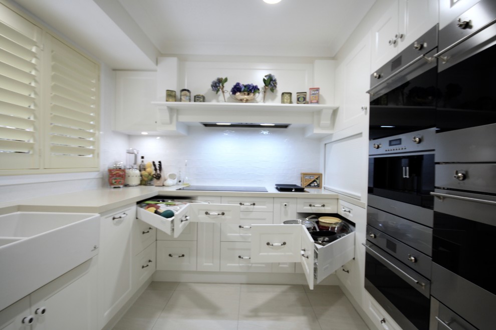 Photo of a large traditional u-shaped open plan kitchen in Sydney with a farmhouse sink, recessed-panel cabinets, white cabinets, quartz benchtops, white splashback, subway tile splashback, stainless steel appliances, ceramic floors, with island, beige floor and beige benchtop.
