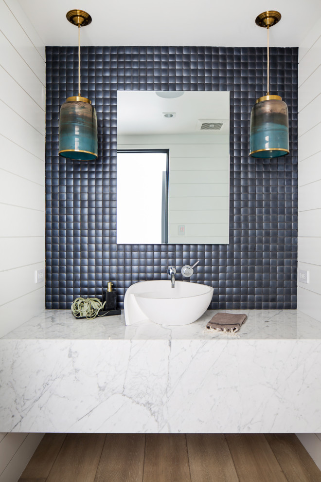 This is an example of a mid-sized beach style 3/4 bathroom in Orange County with white walls, a vessel sink, marble benchtops, white benchtops, white cabinets, blue tile, medium hardwood floors and brown floor.