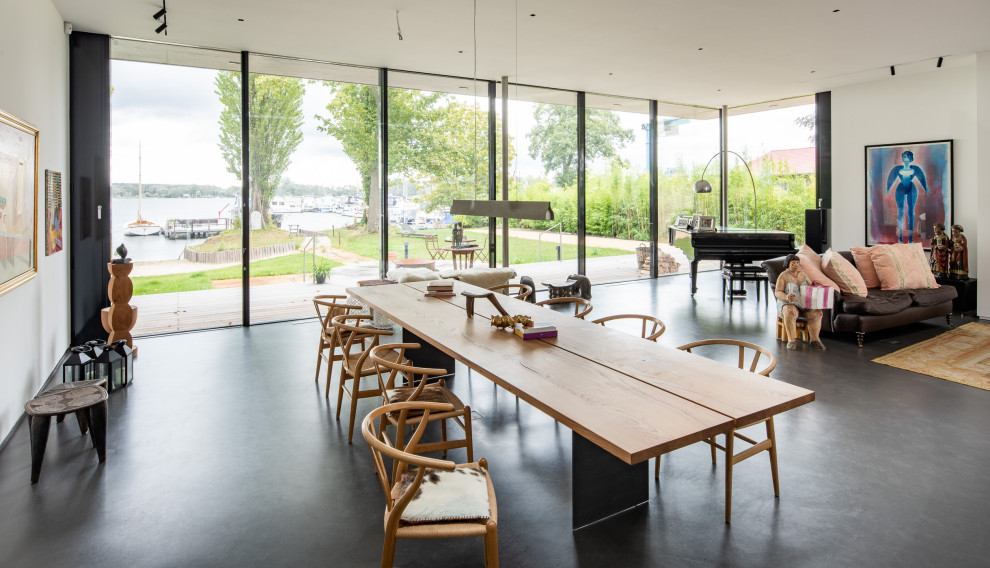 Foto di una sala da pranzo aperta verso il soggiorno minimalista con pareti bianche, pavimento in cemento e pavimento grigio