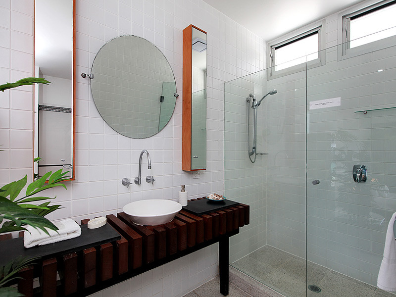 Mid-sized beach style bathroom in Brisbane with raised-panel cabinets, medium wood cabinets, a curbless shower, white tile, porcelain tile, white walls, ceramic floors, a vessel sink and wood benchtops.