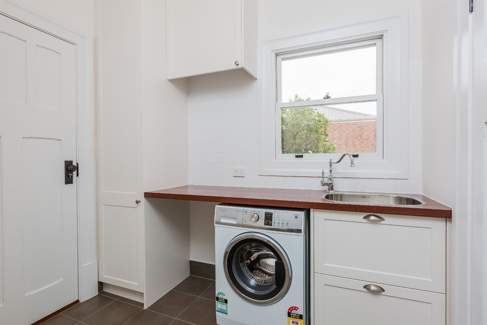 Design ideas for a small country galley dedicated laundry room in Adelaide with a drop-in sink, shaker cabinets, white cabinets, wood benchtops, white walls, ceramic floors, a side-by-side washer and dryer and grey floor.