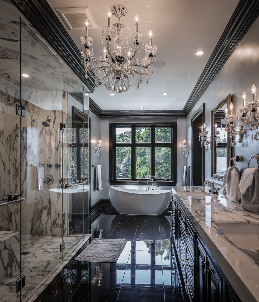 This is an example of a traditional bathroom in Milwaukee with raised-panel cabinets, black cabinets, a freestanding tub, a curbless shower, black and white tile, grey walls, an undermount sink, black floor, a hinged shower door and white benchtops.