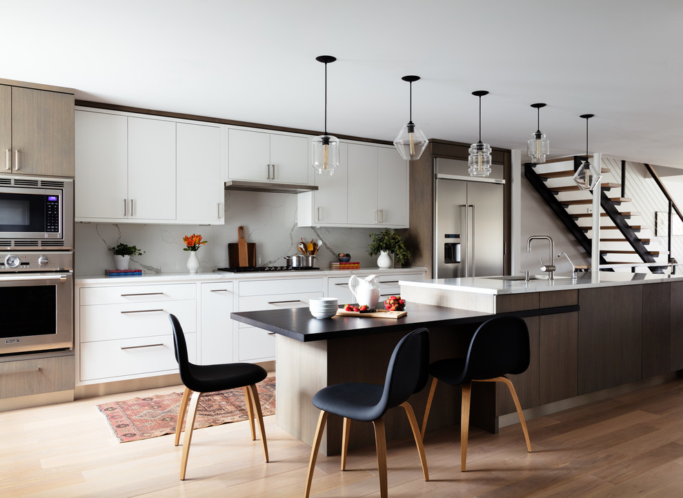 Inspiration for a mid-sized contemporary single-wall open plan kitchen in New York with flat-panel cabinets, light wood cabinets, quartz benchtops, white splashback, marble splashback, stainless steel appliances, light hardwood floors, with island, beige floor and white benchtop.