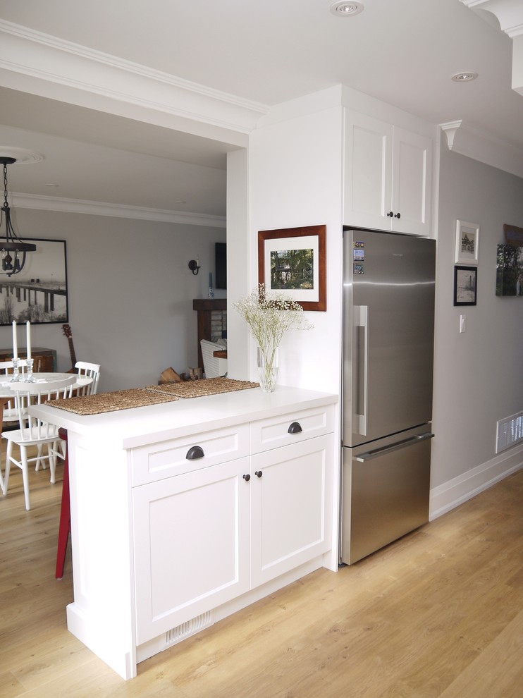 Eat-in kitchen - small transitional l-shaped light wood floor eat-in kitchen idea in Toronto with a farmhouse sink, shaker cabinets, white cabinets, quartz countertops, white backsplash, ceramic backsplash, stainless steel appliances and a peninsula