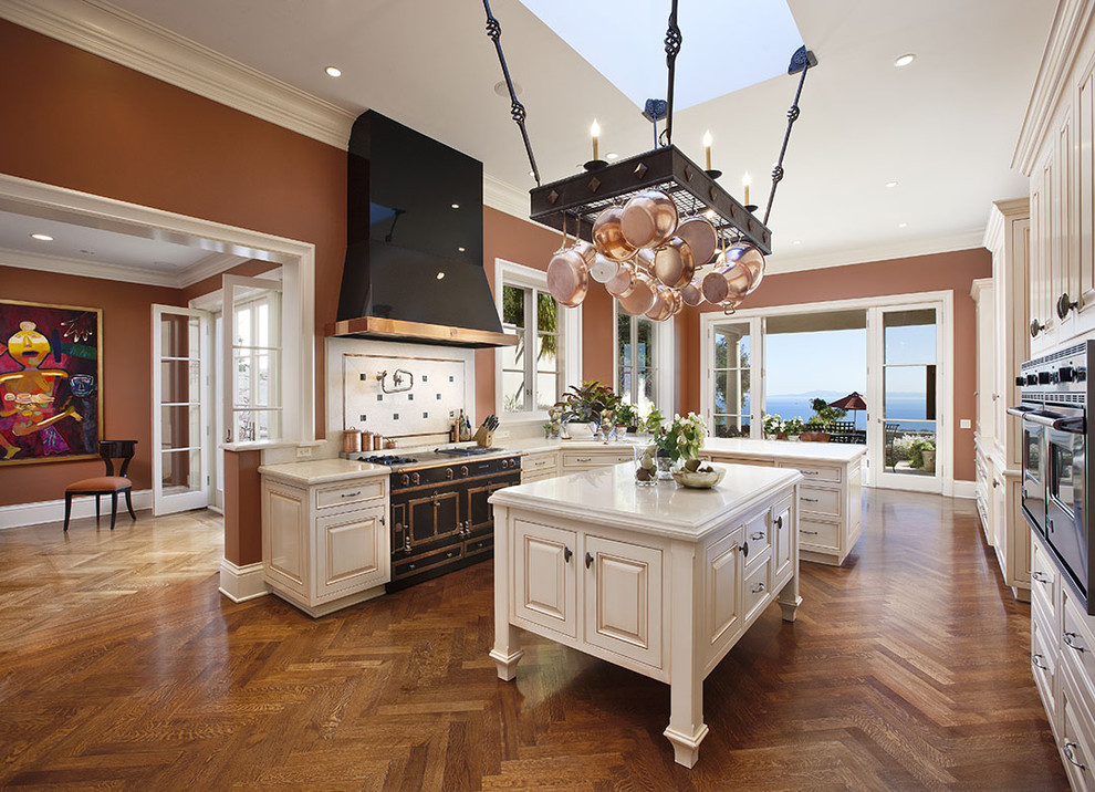 Inspiration for a large mediterranean kitchen in Santa Barbara with raised-panel cabinets, marble benchtops, white cabinets, black appliances, medium hardwood floors and with island.