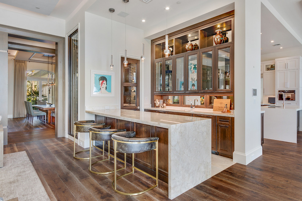 Inspiration for an expansive transitional single-wall wet bar in Miami with medium wood cabinets, marble benchtops, medium hardwood floors, brown floor, an undermount sink, recessed-panel cabinets, mirror splashback and beige benchtop.