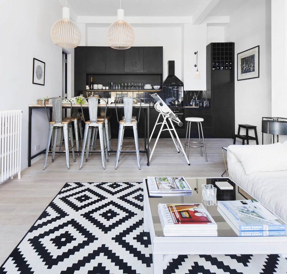 Contemporary single-wall open plan kitchen in London with granite benchtops, black splashback, black appliances and light hardwood floors.