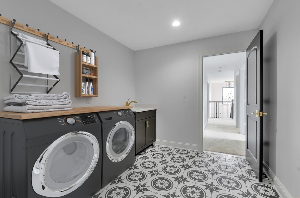 Photo of a medium sized contemporary utility room in New York with black cabinets, grey walls, a side by side washer and dryer, black floors and white worktops.
