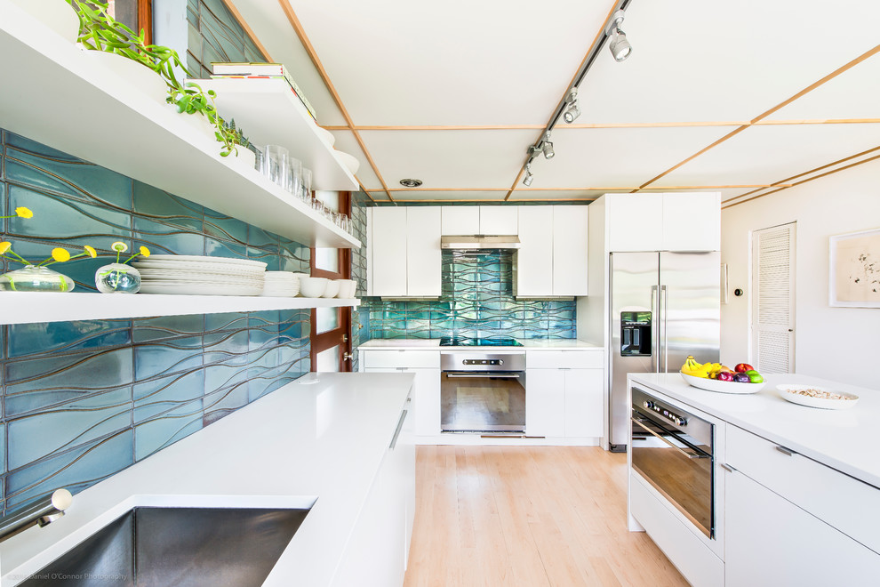 Mid-sized midcentury u-shaped kitchen in Los Angeles with a drop-in sink, flat-panel cabinets, white cabinets, quartz benchtops, blue splashback, ceramic splashback, stainless steel appliances, light hardwood floors and a peninsula.