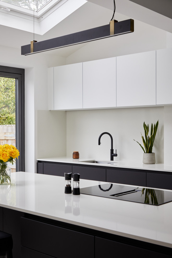 Medium sized modern single-wall kitchen/diner in London with a submerged sink, flat-panel cabinets, black cabinets, engineered stone countertops, white splashback, engineered quartz splashback, stainless steel appliances, an island and white worktops.