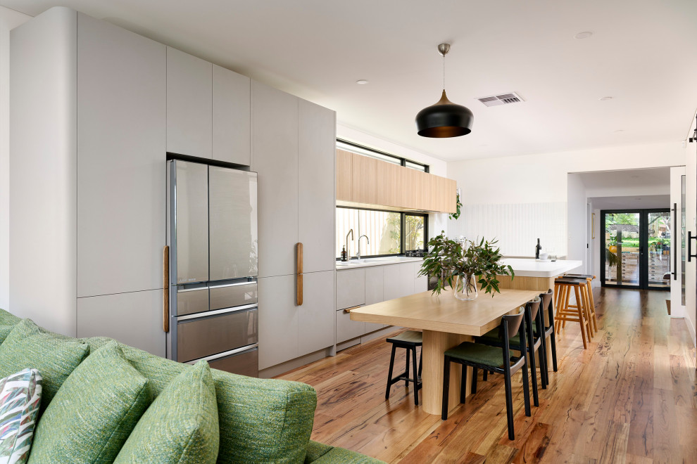 Inspiration for a large scandi galley open plan kitchen in Perth with a double-bowl sink, flat-panel cabinets, grey cabinets, engineered stone countertops, white splashback, mosaic tiled splashback, black appliances, medium hardwood flooring, an island, brown floors and white worktops.