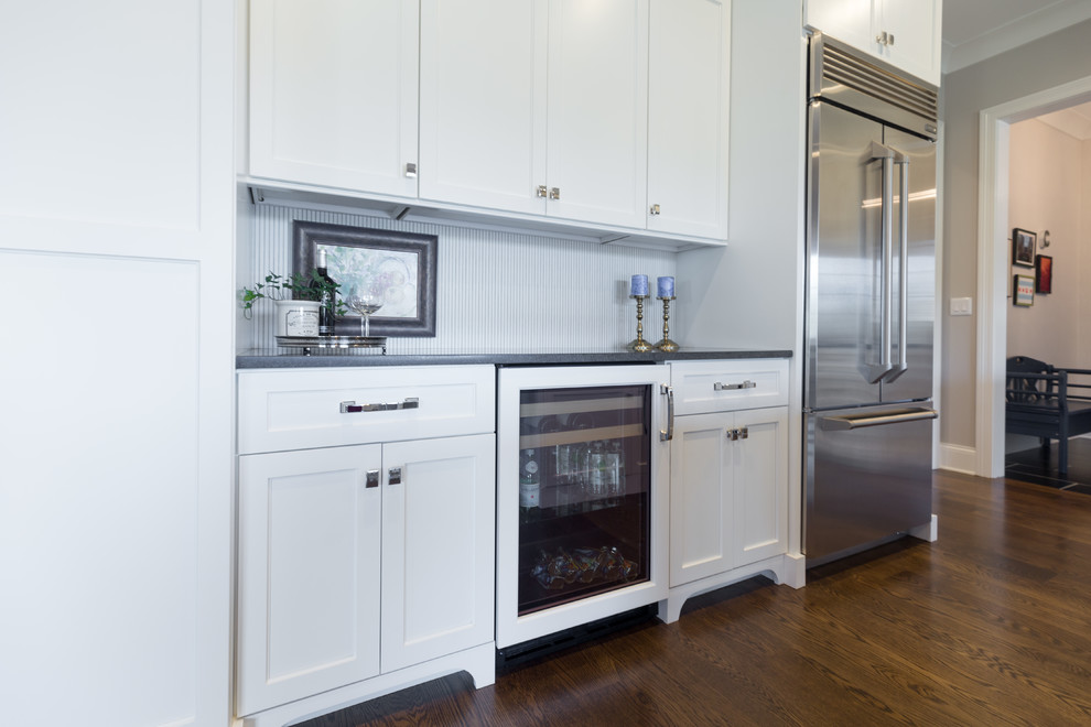 Inspiration for a large transitional u-shaped dark wood floor and brown floor kitchen remodel in Chicago with an undermount sink, shaker cabinets, white cabinets, solid surface countertops, white backsplash, ceramic backsplash, stainless steel appliances, an island and black countertops