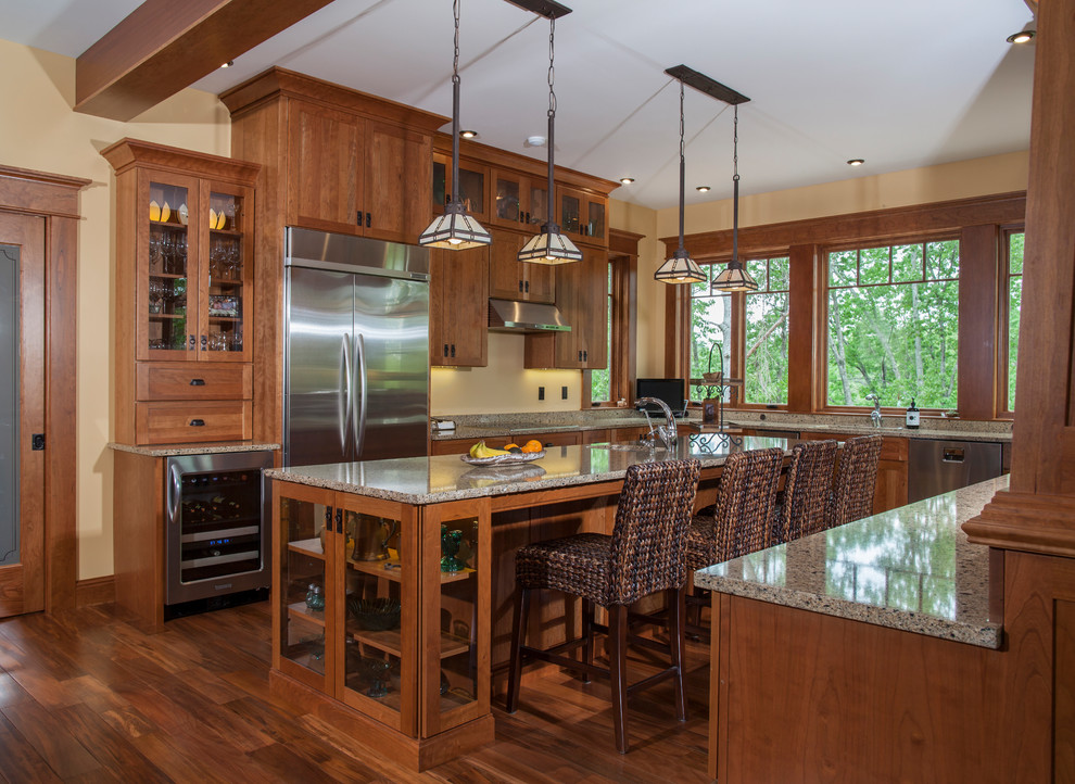 Photo of a mid-sized traditional u-shaped kitchen in Portland Maine with medium wood cabinets, granite benchtops, stainless steel appliances, medium hardwood floors, with island, brown floor, an undermount sink, recessed-panel cabinets, brown splashback, granite splashback, brown benchtop and exposed beam.