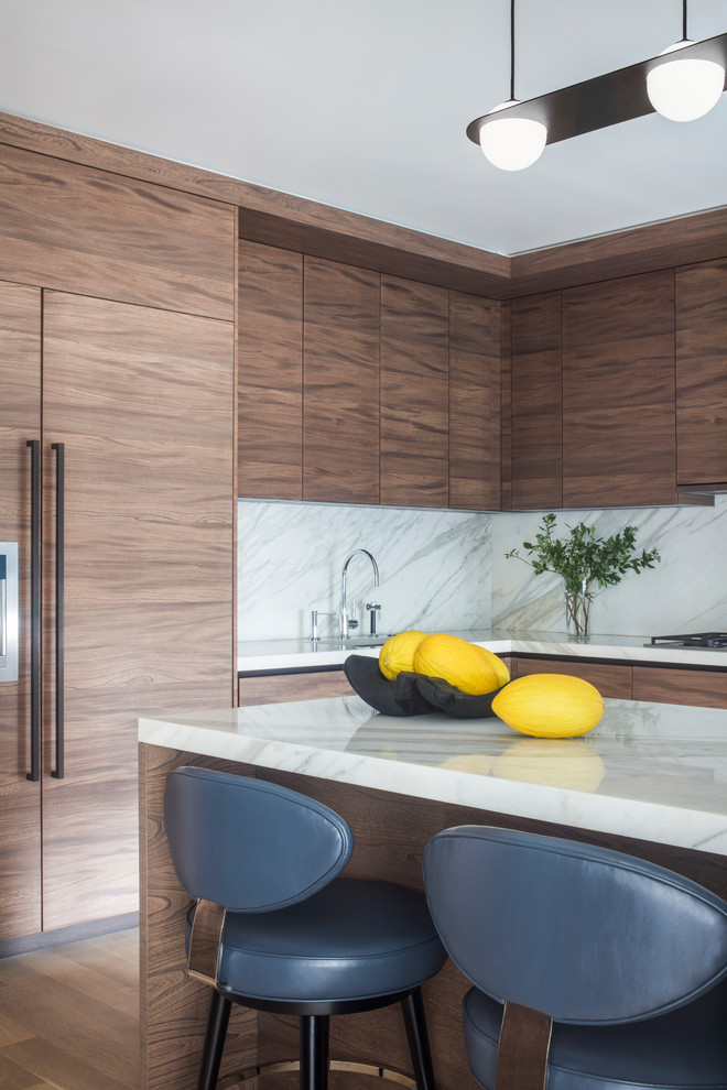 This is an example of a contemporary l-shaped kitchen in New York with an undermount sink, flat-panel cabinets, dark wood cabinets, white splashback, stone slab splashback, panelled appliances, with island and white benchtop.