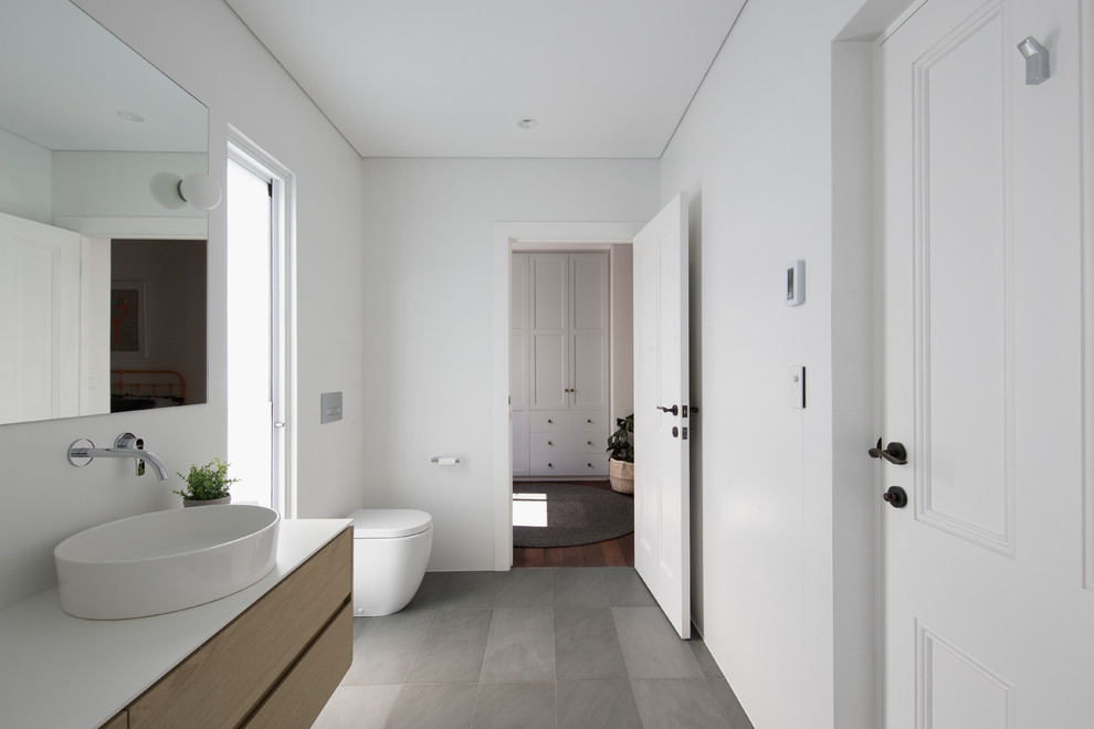 This is an example of a contemporary kids bathroom in Perth with open cabinets, light wood cabinets, a wall-mount toilet, white tile, ceramic tile, white walls, slate floors, a vessel sink, tile benchtops, grey floor and white benchtops.