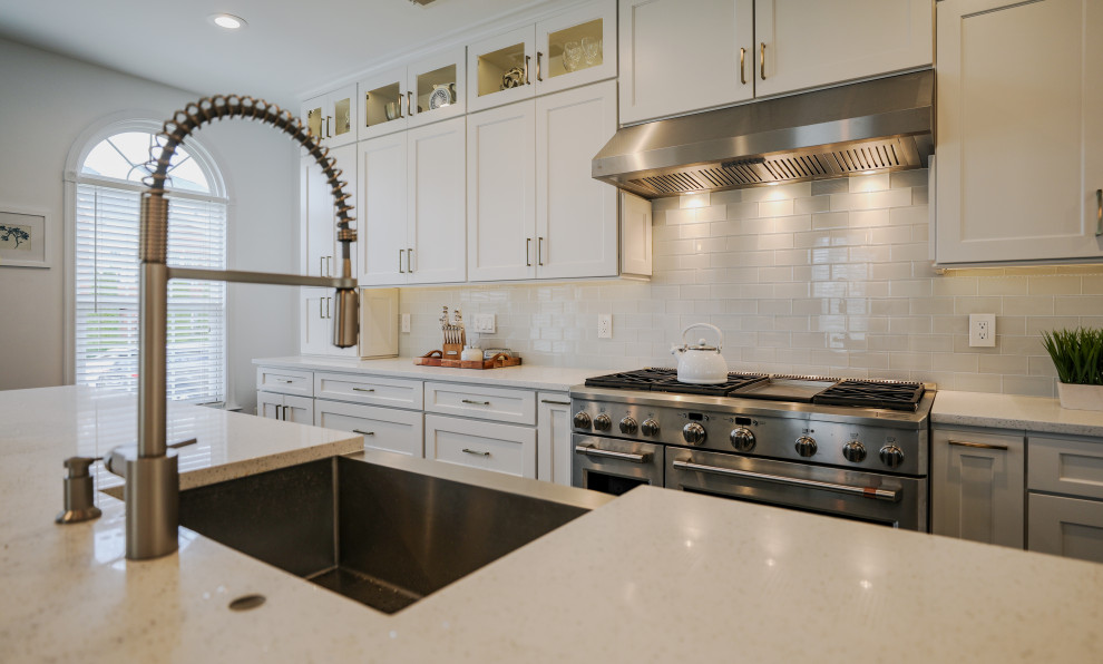 Example of a large minimalist kitchen design in DC Metro with a farmhouse sink, white cabinets, quartzite countertops, white backsplash, glass tile backsplash, stainless steel appliances, an island and white countertops